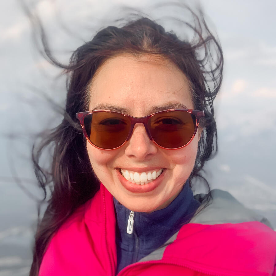 Layla Messner Headshot of autistic founder Layla Messner with her hair blowing in the wind. A brunette in a fuscia jacket and sunglasses.